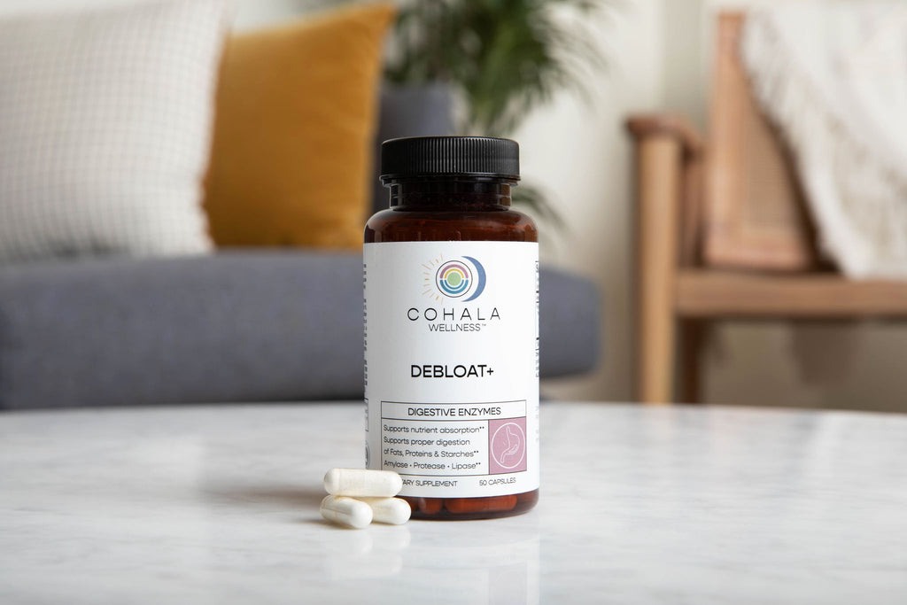 COHALA Wellness Debloat+ digestive enzyme bottle with white capsules on a marble table in a living room