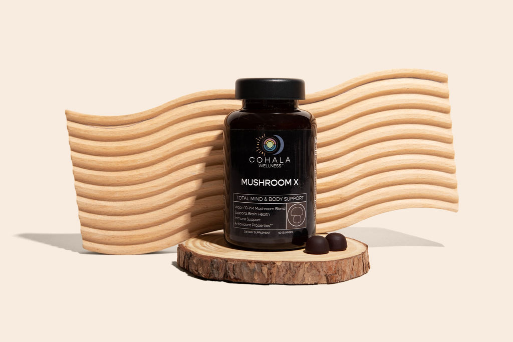 COHALA Wellness Mushroom X supplement bottle on a wood slice in front of a wavy wooden backdrop